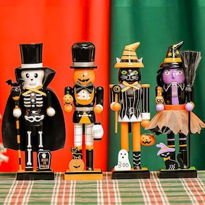 May include: Four Halloween-themed nutcrackers. A skeleton, a pumpkin-headed figure, a black cat, and a witch. Each nutcracker is painted with black, orange, and white details. The witch has a purple face and a broom. The cat has a striped outfit.