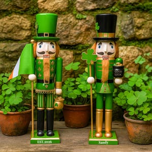 Peut inclure: Deux casse-noisettes en bois avec des détails peints. La figurine de gauche porte un haut-de-forme vert, tient un drapeau vert, blanc et orange, et possède une base marquée EST.2026. La figurine de droite porte un haut-de-forme noir, tient un trèfle vert et a une base marquée Sandy.