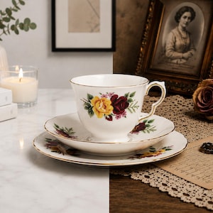 May include: A fine bone china teacup and saucer set, decorated with yellow and burgundy roses. The set is on a marble surface, with a lit candle and books in the background. The teacup has a gold trim.