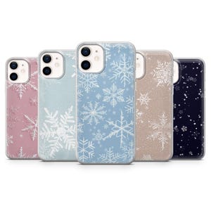 Peut inclure: Cinq coques de téléphone avec des motifs de flocons de neige. Les coques sont de différentes couleurs : rose, bleu clair, bleu, beige et bleu marine. Chaque coque a un bord transparent et un motif de flocon de neige blanc différent.