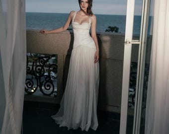 May include: A floor-length white gown featuring a fitted bodice with a sweetheart neckline and thick straps, transitioning into a flowing, pleated skirt. The garment is constructed with a smooth, structured upper section and a sheer, layered lower skirt.