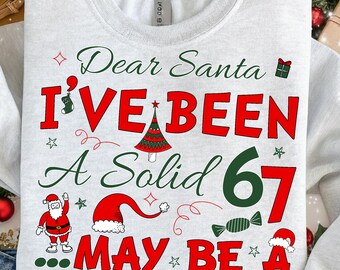 Può includere: Una felpa grigio chiaro con la scritta "Dear Santa I've Been A Solid 67 May Be A" in rosso e verde. Il design include un albero di Natale, Babbo Natale e altre grafiche festive. Le parole "DIGITAL DOWNLOAD FILE" sono in basso.