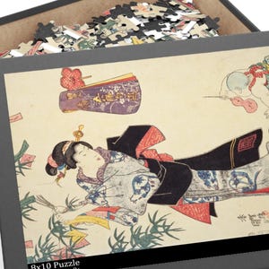以下が含まれることがあります： 黒いパズルボックスが部分的に開いており、日本の芸術作品のパズルが表示されています。イラストは着物を着た女性を描いています。ボックスには「8x10 Puzzle」、「120個、年齢9+」と記載されています。パズルのピースが見えます。