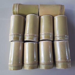 May include: A set of ten bamboo drinking cups. The cups are all the same size and shape, and they are made of natural bamboo. The cups are arranged in a grid pattern, with three rows of three cups and one row of four cups.