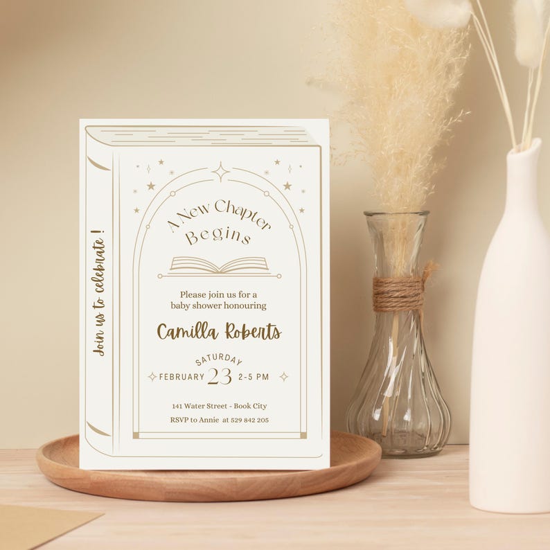May include: A cream-colored baby shower invitation designed to look like a book. The text reads "A New Chapter Begins" and invites guests to celebrate Camilla Roberts. The date is February 23rd, 2-5 PM.