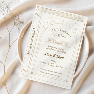 May include: Cream-colored baby shower invitation with a book-themed design. The text reads "A New Chapter Begins" with details for Lisa Bishop's baby shower, including the date, time, and location. The invitation is on a white plate.