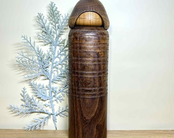 May include: A handcrafted wooden doll with a dark brown, cylindrical body and a lighter brown, rounded head. The body features horizontal carved lines. The doll is a unique decorative item.
