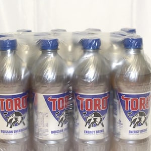 Może przedstawiać: 12-pak srebrnych puszek napoju energetycznego Toro. Puszkie mają niebiesko-czerwoną etykietę z logo byka i tekstem "Toro Nap&oacute;j Energetyczny".