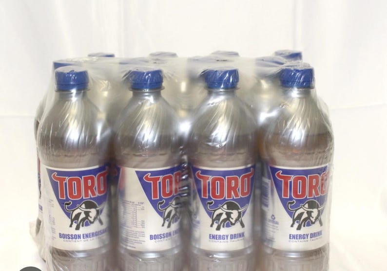 Może przedstawiać: 12-pak srebrnych puszek napoju energetycznego Toro. Puszkie mają niebiesko-czerwoną etykietę z logo byka i tekstem "Toro Nap&oacute;j Energetyczny".