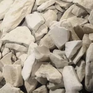May include: A pile of irregularly shaped, off-white rocks. The rocks vary in size and have a slightly rough texture. The lighting creates subtle shadows, adding depth to the arrangement. The overall impression is of a natural, earthy material.