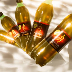 May include: Several bottles of Ragaman energy drink are arranged diagonally. The bottles are filled with a yellow-green liquid and have a dark red label with gold lettering. The bottle caps are green and brown. The background is white.