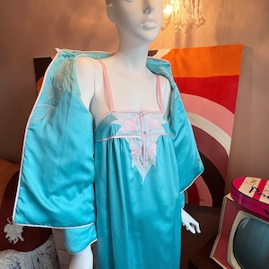 Puede incluir: Un camisón de satén turquesa con un diseño de bordado floral rosa. El camisón tiene una bata a juego con ribete blanco.