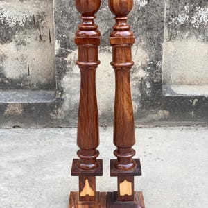 May include: Two wooden balusters with a dark brown finish. Each baluster has a rounded top, a turned central column, and a square base with decorative inlays. These balusters are designed for architectural or decorative purposes.