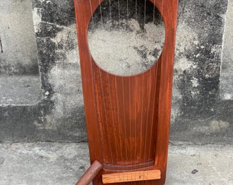 May include: A handcrafted, wooden lyre with a rich, reddish-brown finish. The instrument features a large circular sound hole and multiple strings. A tuning tool rests beside the lyre. The lyre is a stringed musical instrument.