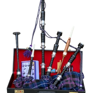 Puede incluir: Un juego de gaita en un estuche negro, con detalles plateados, borlas moradas y una bolsa de tartán morado y azul. El juego incluye un puntero, zánganos y otras piezas, sobre un fondo rojo.
