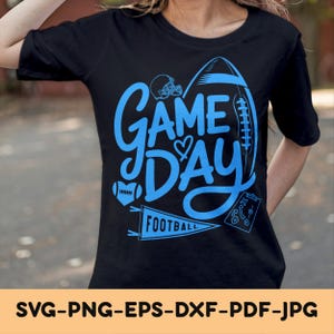 Puede incluir: Camiseta negra con un diseño azul de "Game Day" que presenta un balón de fútbol, un casco y un diagrama de juego. La palabra "Football" está en una banderín. Es una prenda informal.