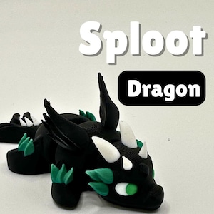 May include: A black dragon figurine with white horns and green accents. The dragon is lying down, with the word "Sploot" above it and "Dragon" in a black box. The dragon has green eyes and is on a white background.