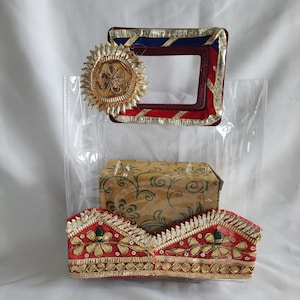 May include: An assortment of decorative items, including a red, blue, and gold framed square, a gold floral embellishment, and two red and gold headpieces. A small, patterned box is also visible, all within a clear plastic bag.