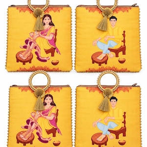 May include: Four square yellow fabric handbags featuring illustrations of individuals in traditional attire. Each bag has a circular handle adorned with small white beads and a gold tassel. The prints depict people seated on wooden stools with henna designs.