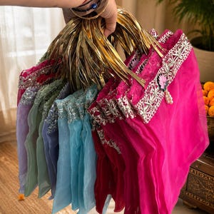 May include: A collection of sheer organza pouches in vibrant shades of hot pink, light blue, lavender, and sage green. Each pouch features a metallic gold circular handle, a decorative silver lace trim along the top edge, and a small floral charm.