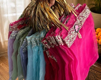 May include: A collection of sheer organza pouches in vibrant shades of hot pink, light blue, lavender, and sage green. Each pouch features a metallic gold circular handle, a decorative silver lace trim along the top edge, and a small floral charm.