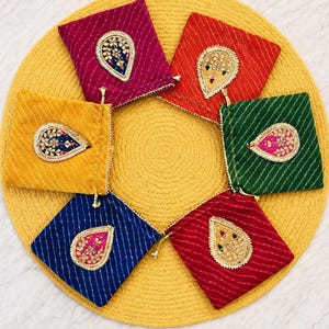 May include: Six square fabric pouches in magenta, orange, green, yellow, blue, and red, each featuring a diagonal striped pattern and a central teardrop-shaped embroidered patch with metallic gold thread and colorful bead accents.