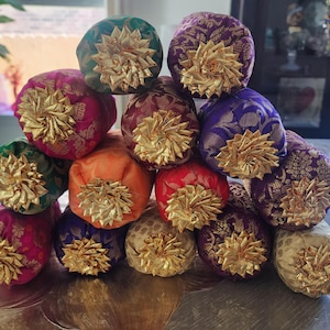 May include: A collection of colorful, decorative fabric balls. Each ball is a different color, including green, pink, orange, red, purple, and gold. They are adorned with a gold, starburst-shaped embellishment.
