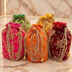 May include: A collection of five drawstring pouches in bright pink, orange, deep red, green, and yellow. Each pouch features intricate gold floral embroidery and is adorned with long, dangling white pearl bead strands and gold-toned metal tassels.