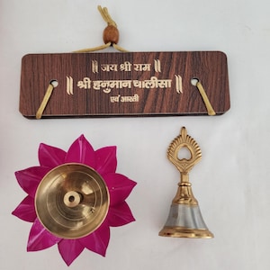 May include: A wooden plaque with gold text and a hanging cord, a pink lotus-shaped oil lamp, and a gold and silver bell. The plaque has text in a foreign language. The oil lamp has a gold interior. The bell has a decorative handle.