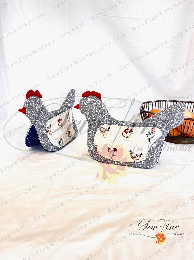 May include: Two chicken-shaped oven mitts. The mitts are gray with a white and gray floral pattern. The front of the mitts have a white background with chicken illustrations. The chickens have red combs and beaks. The mitts have red bows on top.