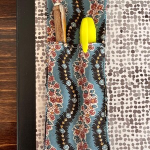 Puede incluir: Un cuaderno con un bolsillo estampado floral, que contiene un bol&iacute;grafo y un resaltador amarillo. El bolsillo tiene un fondo azul con un dise&ntilde;o floral. El texto "Flower Chain" est&aacute; en la parte inferior.