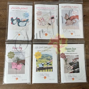 May include: Six individual sewing pattern booklets for oven mitts in clear plastic sleeves. The patterns are titled Henrietta Hotmitt, Betsy Bunny Oven Mitt, Mabel Kitty Mittens, Piper Pig, Lily Lamb Oven Mitt, and Clover Cow Oven Mitt by Sew Fine.