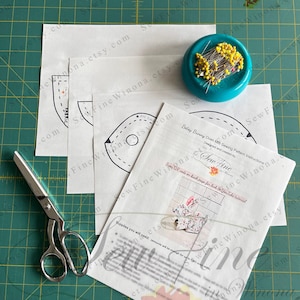 Peut inclure: Une composition de couture avec des patrons, des ciseaux et un coussin &agrave; &eacute;pingles. Le patron comprend des instructions pour un "Betay Bunny Oven Mitt". L'image est sur un tapis de coupe vert.