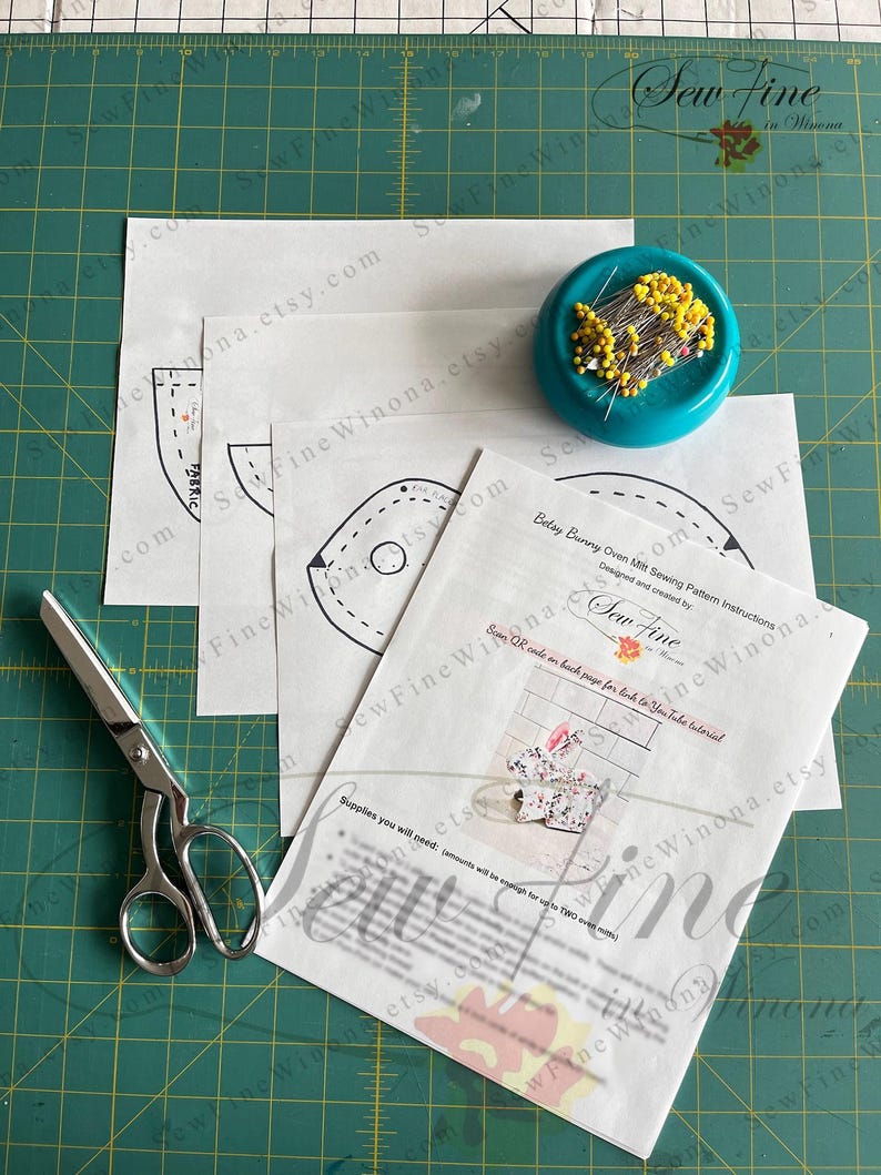 Peut inclure: Une composition de couture avec des patrons, des ciseaux et un coussin &agrave; &eacute;pingles. Le patron comprend des instructions pour un "Betay Bunny Oven Mitt". L'image est sur un tapis de coupe vert.