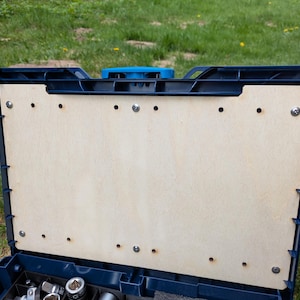 Puede incluir: Una caja de herramientas de plástico azul con un inserto de madera. El inserto tiene varios agujeros para guardar herramientas.