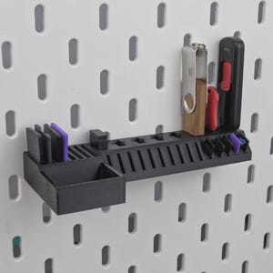 Peut inclure: Une étagère organisatrice noire en plastique pour panneau perforé, comprenant un bac de rangement rectangulaire sur la gauche, une série de fentes verticales pour petits objets et une longue rangée horizontale d'encoches pour divers outils.