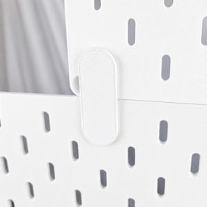 Puede incluir: Un panel perforado blanco con un patrón repetitivo de aberturas ovaladas verticales. Una pieza de conexión ovalada blanca está fijada en la parte frontal, superponiéndose a la unión entre dos secciones apiladas del panel perforado.