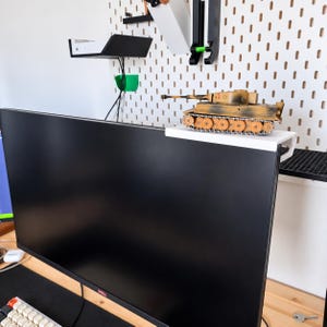Könnte beinhalten: Eine weiße Monitor-Ablage aus Kunststoff, die am oberen Rand eines schwarzen Dell-Computermonitors befestigt ist. Ein kleines, detailliertes Modell eines beigefarbenen und braunen Militärpanzers mit langem Rohr und Rädern steht auf der Ablage.