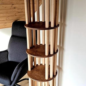 May include: A four-tiered wooden shelf unit with a dark brown top and shelves, supported by light-coloured wooden dowels. The unit is cylindrical and stands tall, showcasing a modern design. The shelves are approximately 30 cm in diameter.