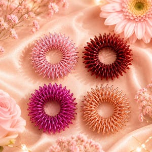 Könnte beinhalten: Vier kreisförmige Haarspiralen in quadratischer Anordnung. Die Spirale oben links ist hellrosa, oben rechts dunkelrot, unten links magentafarben und unten rechts kupferfarben. Jede Spirale hat ein gewundenes, telefonkabelartiges Design.