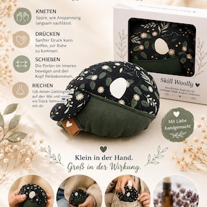 Könnte beinhalten: Ein Skill Woolly sensorisches Wal-Spielzeug mit schwarzem Stoffoberteil mit weiß-grünem Blumenmuster, einfarbig dunkelgrünem Unterteil und weißem ovalen Aufnäher. Die Verpackung zeigt den Text Skill Woolly und beschreibende Symbole zur Anwendung.