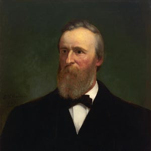 May include: A portrait of a man with a long, reddish-brown beard and graying hair. He wears a black suit with a white shirt and a black bow tie. The background is a dark green.