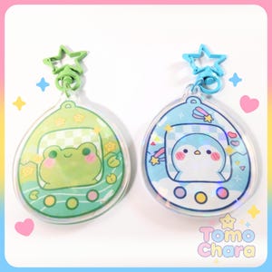 May include: Two clear acrylic keychains with cartoon designs. One features a green frog, the other a blue penguin. Each keychain has a star-shaped clasp and the text "Tomo Chara".