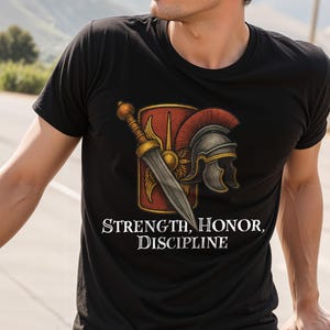 Può includere: T-shirt nera con grafica a tema romano: scudo, elmo e spada. Il testo "STRENGTH, HONOR, DISCIPLINE" è in bianco. La maglietta ha girocollo e maniche corte.