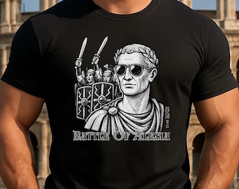 May include: Black t-shirt featuring a graphic of a Roman emperor wearing sunglasses and a laurel wreath. The image includes the text "BATTLE OF ALESIA" and a depiction of Roman soldiers. The shirt is worn by a person.