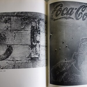May include: A monochrome photograph of two open book pages. The left page features a large numeral on a brick wall. The right page shows the Coca-Cola logo. The text "THE BEAUTY - UGLINESS OF TIME - 1945" is visible.