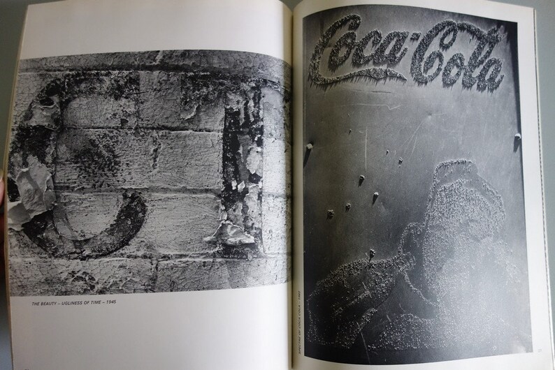 May include: A monochrome photograph of two open book pages. The left page features a large numeral on a brick wall. The right page shows the Coca-Cola logo. The text "THE BEAUTY - UGLINESS OF TIME - 1945" is visible.