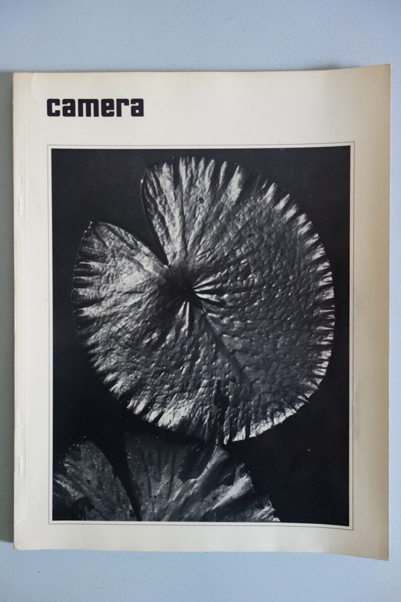 May include: A monochrome photograph of a magazine cover. The image shows a detailed view of a lily pad. The word "camera" is printed in bold, black letters at the top of the cover.