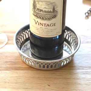 May include: A wine bottle with a "Vintage" label sits in a silver coaster, next to a wine glass filled with red wine. A cork and a corkscrew are also visible on the wooden surface. The scene suggests a wine tasting or a dining setting.