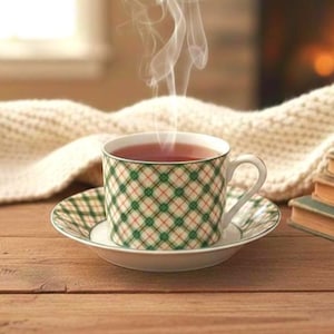 May include: A cup of tea with steam rising, set on a saucer. The cup and saucer have a green and white plaid pattern. The tea is a deep red color. The scene is set on a wooden table with a cozy blanket and books.